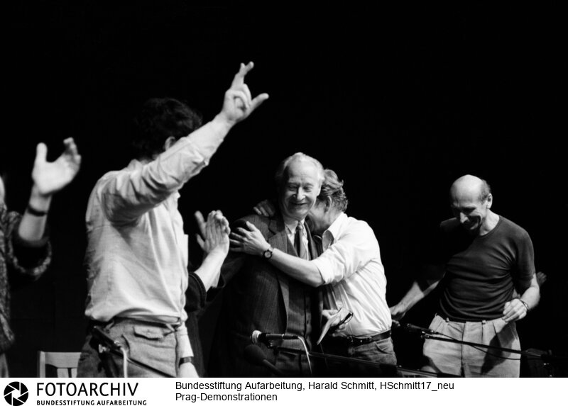 Alexander Dubcek (l.), Leitfigur des Prager Frühlings 1968, und Vaclav Havel, Schriftsteller und prominentester Regimegegner, auf dem Podium des Bürgerforums am 24. November. Aus dem Publikum wird ihnen zugerufen, dass der Prager Vorsitzende der Kommunistischen Partei zurückgetreten ist. Dubcek und Havel springen auf und umarmen sich. Sie wissen: Das Regime ist am Ende, das ist ihr Sieg. <BR>Aufnahmedatum: 24.11.1989<BR>Material/Technik: Foto<BR>Aufnahmeort: Prag / Tschechoslowakei (Tschechien)<BR>Signatur: HSchmitt17_neu