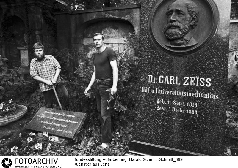 Der Bildhauer Lutz Leibner (links) und der Maler Frank Rub sind 1979 an einer Ausstellung in der Jenaer Stadtkirche unter dem Motto "Hoffnung, Glaube, Humanismus" beteiligt. Ihre Exponate sind Proteste. Sie zeigen Tunnelkriecher, Schnüffelschnauzen, Knüppelmänner. Sie müssen abgehängt werden. Die Künstler verlieren ihre Arbeit und jobben jetzt auf dem Friedhof. Film: 82 0620  Negativ: 14a.<BR>Person: Rub, Frank, [1952 - ], deutscher Maler und Bildhauer, Aktivist der Jenaer Friedensgemeinde Leibner, Lutz, [1949 - ], deutscher Bildhauer und DDR-Oppositioneller Zeiss, Carl, [11.9.1816 - 3.12.1888], deutscher Unternehmer<BR>Aufnahmedatum: 1982<BR>Material/Technik: Foto<BR>Aufnahmeort: Jena / DDR (Deutschland)<BR>Signatur: Schmitt_369