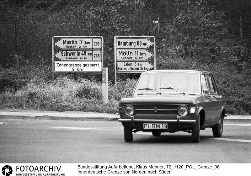 Landkreis Lauenburg (Schleswig-Holstein), 20-11-1972. Seit dem Bau der Mauer hat die Deutsche Demokratische Republik (DDR) die Demarkationslinie entlang ihrer Staatsgrenze West optimiert. Die Geländeanpassung der Zonengrenze zementiert die Teilung Deutschlands, für Flüchtlinge besteht Lebensgefahr. Das durch Grenzsoldaten bewachte Sperrsystem ist durch Todesstreifen, Minen und Wachtürme abgeriegelt. Foto: Wegweiser zu Orten in der DDR bei Ratzeburg. Sign post to villages in East-Germany near Ratzeburg.<BR>Material/Technik: Foto<BR>Schleswig-Holstein<BR>Signatur: 72_1120_POL_Grenze_06