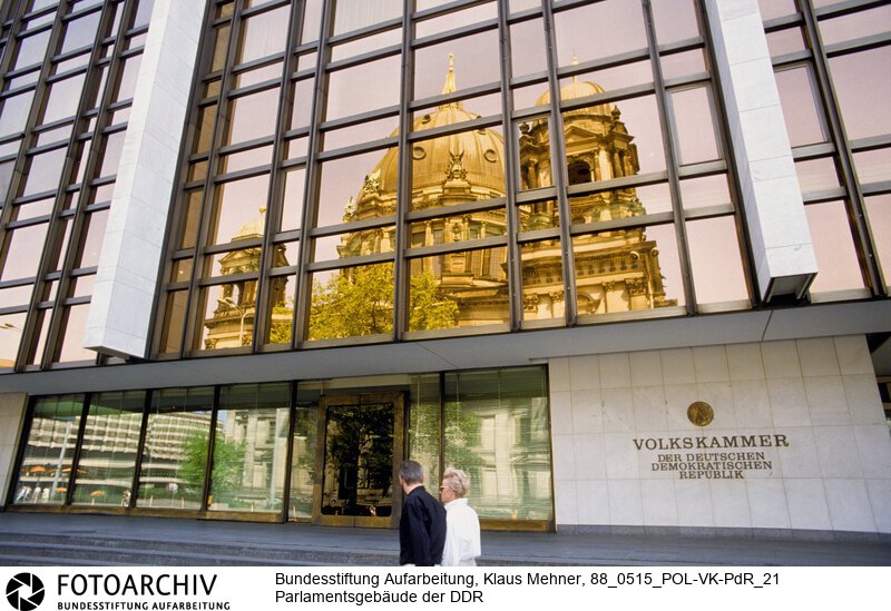 Berlin (Bezirk Berlin) DDR, 15-05-1988. Sitz der DDR-Volkskammer. Das Parlament der Deutschen Demokratischen Republik (DDR) residiert im Palast der Republik (PdR). Der nördliche Teil von Erichs Lampenladen (Volksmund) ist den Abgeordneten der Volkskammer vorbehalten. Foto: Der liebe Gott sieht Alles; in der Thermoverglasung spiegelt sich der Berliner Dom.<BR>Material/Technik: Foto<BR>Bezirk Berlin<BR>Signatur: 88_0515_POL-VK-PdR_21
