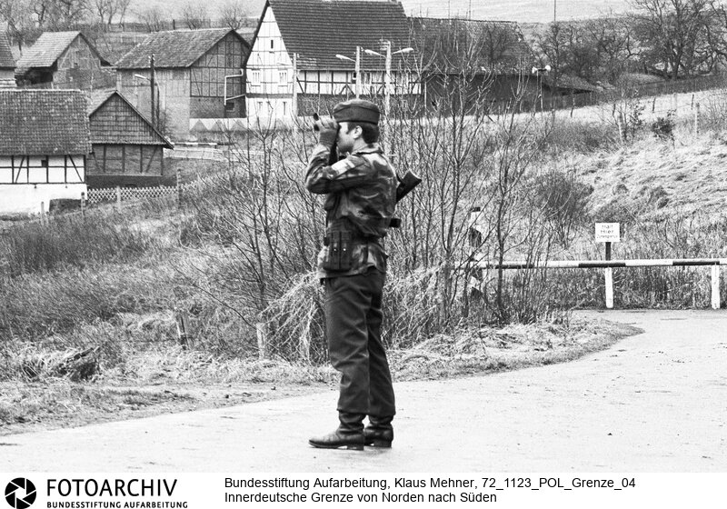 Landkreis Göttingen (Niedersachsen), 23. 11. 1972. Seit dem Bau der Mauer hat die Deutsche Demokratische Republik (DDR) die Demarkationslinie entlang ihrer Staatsgrenze West optimiert. Die dem Gelände angepasste Zonengrenze zementiert die Teilung Deutschlands, für Flüchtlinge besteht Lebensgefahr. Das durch Grenzsoldaten bewachte Sperrsystem ist durch Minen, Todesstreifen und Wachtürme abgeriegelt. Foto: Patrouille des Bundesgrenzschutz (BGS) vor Glasehausen in der DDR. Patrol of West German border guard in front of Glasehausen.<BR>Material/Technik: Foto<BR>Niedersachen<BR>Signatur: 72_1123_POL_Grenze_04