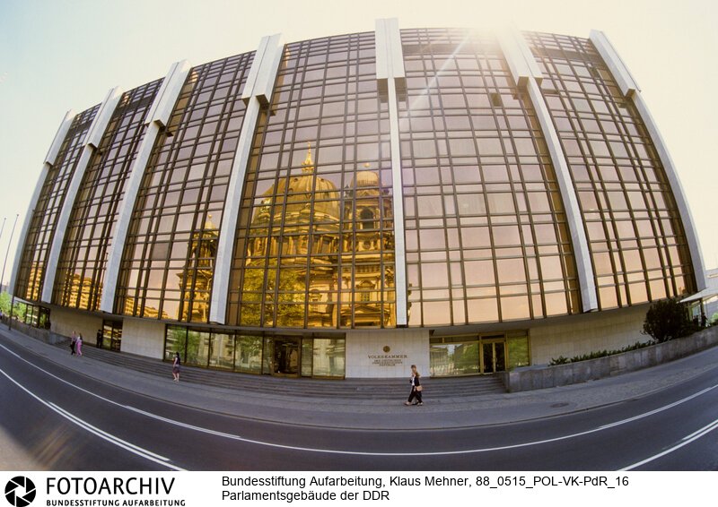 Berlin (Bezirk Berlin) DDR, 15-05-1988. Sitz der DDR-Volkskammer. Das Parlament der Deutschen Demokratischen Republik (DDR) residiert im Palast der Republik (PdR). Der nördliche Teil von Erichs Lampenladen (Volksmund) ist den Abgeordneten der Volkskammer vorbehalten. Foto: Der liebe Gott sieht Alles; in der Thermoverglasung spiegelt sich der Berliner Dom.<BR>Material/Technik: Foto<BR>Bezirk Berlin<BR>Signatur: 88_0515_POL-VK-PdR_16