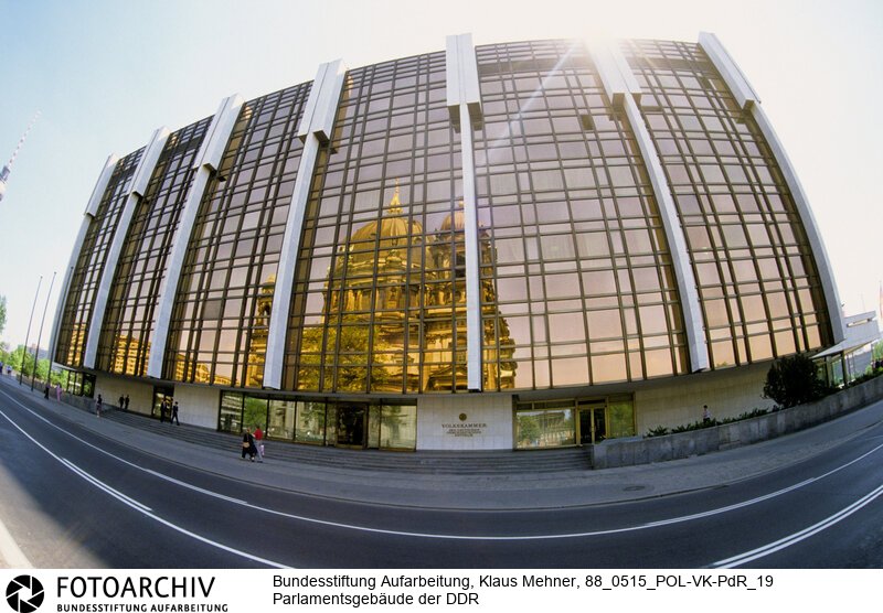 Berlin (Bezirk Berlin) DDR, 15-05-1988. Sitz der DDR-Volkskammer. Das Parlament der Deutschen Demokratischen Republik (DDR) residiert im Palast der Republik (PdR). Der nördliche Teil von Erichs Lampenladen (Volksmund) ist den Abgeordneten der Volkskammer vorbehalten. Foto: Der liebe Gott sieht Alles; in der Thermoverglasung spiegelt sich der Berliner Dom.<BR>Material/Technik: Foto<BR>Bezirk Berlin<BR>Signatur: 88_0515_POL-VK-PdR_19