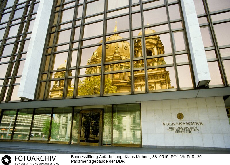 Berlin (Bezirk Berlin) DDR, 15-05-1988. Sitz der DDR-Volkskammer. Das Parlament der Deutschen Demokratischen Republik (DDR) residiert im Palast der Republik (PdR). Der nördliche Teil von Erichs Lampenladen (Volksmund) ist den Abgeordneten der Volkskammer vorbehalten. Foto: Der liebe Gott sieht Alles; in der Thermoverglasung spiegelt sich der Berliner Dom.<BR>Material/Technik: Foto<BR>Bezirk Berlin<BR>Signatur: 88_0515_POL-VK-PdR_20