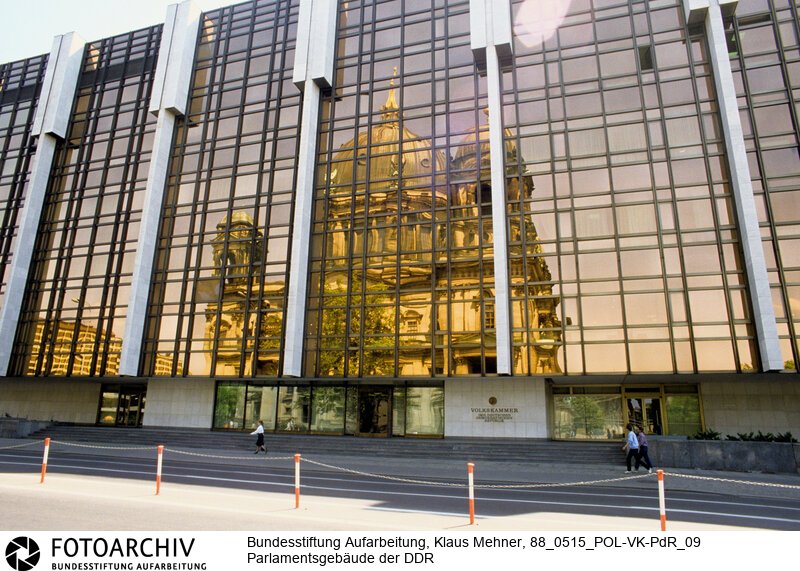 Berlin (Bezirk Berlin) DDR, 15-05-1988. Sitz der DDR-Volkskammer. Das Parlament der Deutschen Demokratischen Republik (DDR) residiert im Palast der Republik (PdR). Der nördliche Teil von Erichs Lampenladen (Volksmund) ist den Abgeordneten der Volkskammer vorbehalten. Foto: Der liebe Gott sieht Alles; in der Thermoverglasung spiegelt sich der Berliner Dom.<BR>Material/Technik: Foto<BR>Bezirk Berlin<BR>Signatur: 88_0515_POL-VK-PdR_09