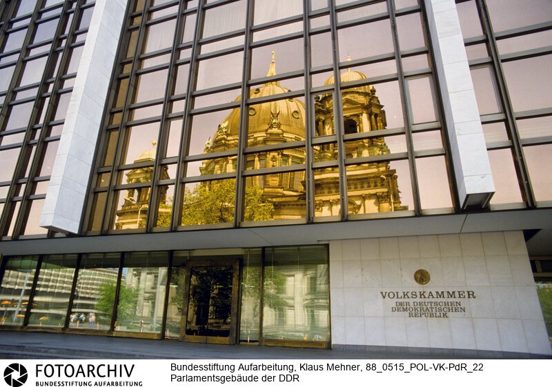 Berlin (Bezirk Berlin) DDR, 15-05-1988. Sitz der DDR-Volkskammer. Das Parlament der Deutschen Demokratischen Republik (DDR) residiert im Palast der Republik (PdR). Der nördliche Teil von Erichs Lampenladen (Volksmund) ist den Abgeordneten der Volkskammer vorbehalten. Foto: Der liebe Gott sieht Alles; in der Thermoverglasung spiegelt sich der Berliner Dom.<BR>Material/Technik: Foto<BR>Bezirk Berlin<BR>Signatur: 88_0515_POL-VK-PdR_22
