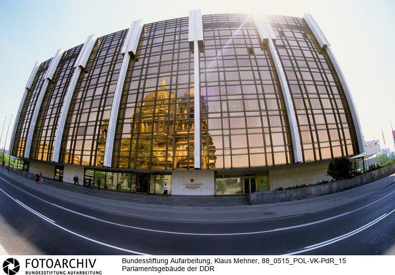 Berlin (Bezirk Berlin) DDR, 15-05-1988. Sitz der DDR-Volkskammer. Das Parlament der Deutschen Demokratischen Republik (DDR) residiert im Palast der Republik (PdR). Der nördliche Teil von Erichs Lampenladen (Volksmund) ist den Abgeordneten der Volkskammer vorbehalten. Foto: Der liebe Gott sieht Alles; in der Thermoverglasung spiegelt sich der Berliner Dom.<BR>Material/Technik: Foto<BR>Bezirk Berlin<BR>Signatur: 88_0515_POL-VK-PdR_15