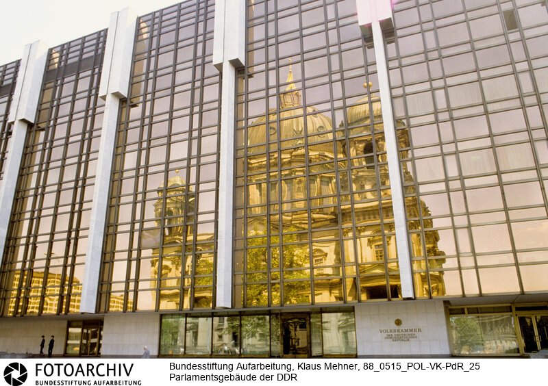 Berlin (Bezirk Berlin) DDR, 15-05-1988. Sitz der DDR-Volkskammer. Das Parlament der Deutschen Demokratischen Republik (DDR) residiert im Palast der Republik (PdR). Der nördliche Teil von Erichs Lampenladen (Volksmund) ist den Abgeordneten der Volkskammer vorbehalten. Foto: Der liebe Gott sieht Alles; in der Thermoverglasung spiegelt sich der Berliner Dom.<BR>Material/Technik: Foto<BR>Bezirk Berlin<BR>Signatur: 88_0515_POL-VK-PdR_25