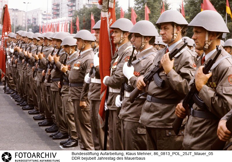 Berlin (Bezirk Berlin) DDR, 13-08-1986. Mit einem Kampfappell der Kampfgruppen (KG) der Arbeiterklasse beging die Deutsche Demokratische Republik (DDR) den 25. Jahrestag des Baus des Antifaschistischen Schutzwalls, vulgo Mauer. Der SED-Chef würdigte das Bauwerk als Voraussetzung für die Friedens- und Entspannungspolitik. Alsdann nahmen Partei- und Staatsführung den Vorbeimarsch von Soldaten der Nationalen Volksarmee (NVA) und Betriebskampfgruppen ab. Foto: Angetretene Kampfgruppen.<BR>Material/Technik: Foto<BR>Bezirk Berlin<BR>Signatur: 86_0813_POL_25JT_Mauer_05