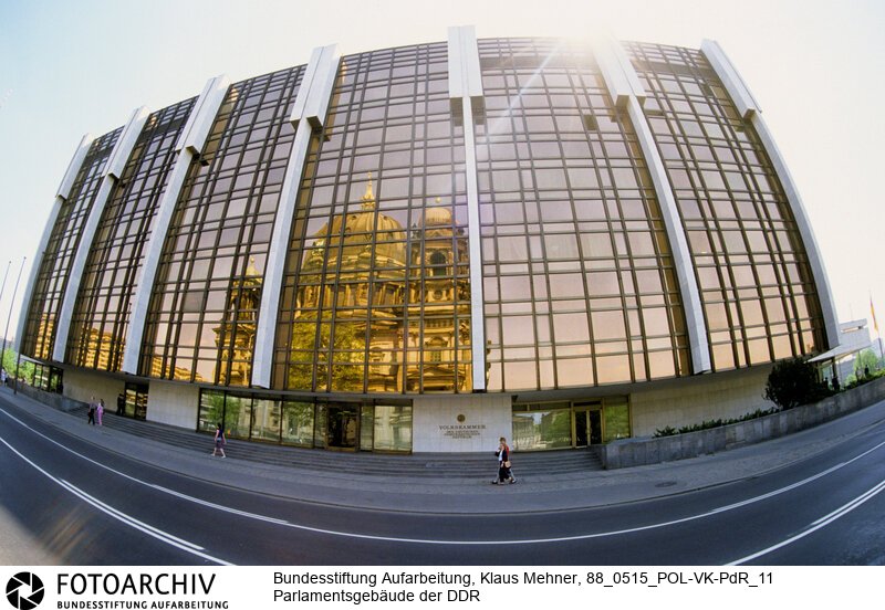 Berlin (Bezirk Berlin) DDR, 15-05-1988. Sitz der DDR-Volkskammer. Das Parlament der Deutschen Demokratischen Republik (DDR) residiert im Palast der Republik (PdR). Der nördliche Teil von Erichs Lampenladen (Volksmund) ist den Abgeordneten der Volkskammer vorbehalten. Foto: Der liebe Gott sieht Alles; in der Thermoverglasung spiegelt sich der Berliner Dom.<BR>Material/Technik: Foto<BR>Bezirk Berlin<BR>Signatur: 88_0515_POL-VK-PdR_11