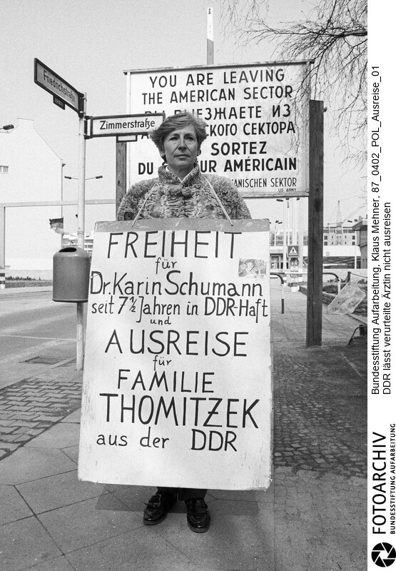 Berlin (Berlin West), 02. 04. 1887. Ost-Berlin lässt verurteilte Ärztin nicht frei. Seit Wochen protestieren der Heidelberger Medizinprofessor Wolf-Dieter und seine Frau Ruth Thomitzek für die Ausreise von Dr. Christa-Karin Schumann vor der Ständigen Vertretung der Deutschen Demokratischen Republik (DDR) in Bonn und an der Mauer am Checkpoint Charlie. Die Schwester des Professors war die Ehefrau von Korvettenkapitän Baumann, BND-Code Roter Admiral, der wegen Spionage verurteilt und hingerichtet wurde. Die Bundesregierung sieht in der Inhaftierung einen Racheakt. Foto: Ruth Thomitzek bei Demonstration am Grenzübergang.<BR>Material/Technik: Foto<BR>Berlin (West)<BR>Signatur: 87_0402_POL_Ausreise_01