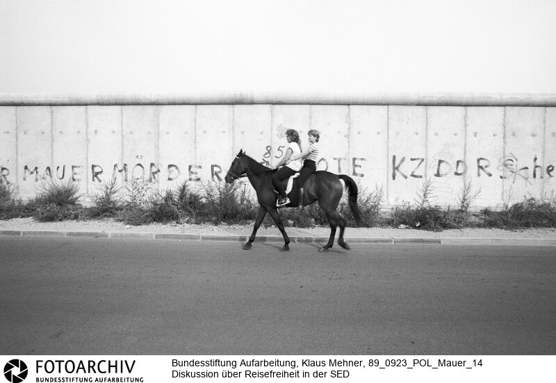 Berlin (Berlin West), 23-09-1989. Diskussion um Reisefreiheit. Über die offene Grenze Ungarns verließen überwiegend junge Familien und Angehörige der technischen Intelligenz die Deutsche Demokratische Republik (DDR). Unter hochrangigen Funktionären der SED (Sozialistischen Einheitspartei) wird der Aderlass und über Reisefreiheit diskutiert. Bilder der Berliner Mauer mit einem Spezialweitwinkel Objektiv. Foto: Frauen zu Pferde auf dem Gelände des Güterbahnhofs Eberswalder Strasse.<BR>Material/Technik: Foto<BR>Berlin (West)<BR>Signatur: 89_0923_POL_Mauer_14