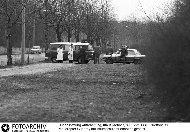 Berlin (Bezirk Berlin) DDR, 23. 02. 1989. Das letzte Opfer des Schießbefehls an der Staatsgrenze der Deutschen Demokratischen Republik (DDR), Chris Gueffroy starb in der Nacht zum 06. Februar 1989 durch Schüsse von Grenzposten bei einem Fluchtversuch an der Berliner Mauer. Die Beisetzung fand auf dem Baumschulenweg-Friedhof statt. Ein Grossaufgebot von Kräften des Ministeriums für Staatssicherheit (MfS, Stasi) und der Volkspolizei (VP, VoPo) schirmte die Trauernden ab. Foto: Volkspolizei am Friedhof.<BR>Material/Technik: Foto<BR>Bezirk Berlin<BR>Signatur: 89_0223_POL_Gueffroy_11