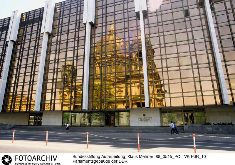 Berlin (Bezirk Berlin) DDR, 15-05-1988. Sitz der DDR-Volkskammer. Das Parlament der Deutschen Demokratischen Republik (DDR) residiert im Palast der Republik (PdR). Der nördliche Teil von Erichs Lampenladen (Volksmund) ist den Abgeordneten der Volkskammer vorbehalten. Foto: Der liebe Gott sieht Alles; in der Thermoverglasung spiegelt sich der Berliner Dom.<BR>Material/Technik: Foto<BR>Bezirk Berlin<BR>Signatur: 88_0515_POL-VK-PdR_10