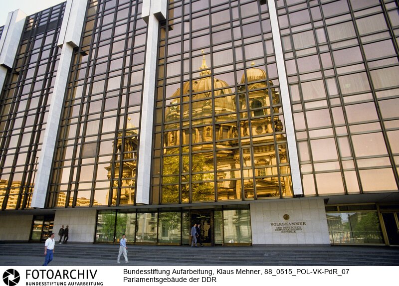 Berlin (Bezirk Berlin) DDR, 15-05-1988. Sitz der DDR-Volkskammer. Das Parlament der Deutschen Demokratischen Republik (DDR) residiert im Palast der Republik (PdR). Der nördliche Teil von Erichs Lampenladen (Volksmund) ist den Abgeordneten der Volkskammer vorbehalten. Foto: Der liebe Gott sieht Alles; in der Thermoverglasung spiegelt sich der Berliner Dom.<BR>Material/Technik: Foto<BR>Bezirk Berlin<BR>Signatur: 88_0515_POL-VK-PdR_07