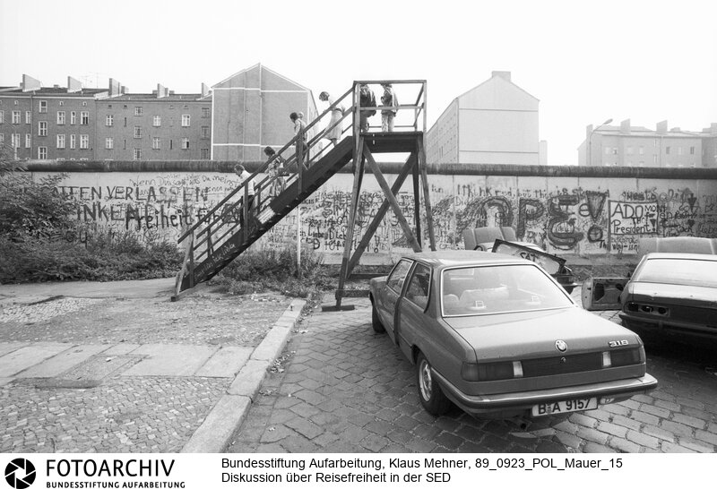 Berlin (Berlin West), 23-09-1989. Diskussion um Reisefreiheit. Über die offene Grenze Ungarns verließen überwiegend junge Familien und Angehörige der technischen Intelligenz die Deutsche Demokratische Republik (DDR). Unter hochrangigen Funktionären der SED (Sozialistischen Einheitspartei) wird der Aderlass und über Reisefreiheit diskutiert. Bilder der Berliner Mauer mit einem Spezialweitwinkel Objektiv. Foto: Besucher auf Aussichtsplattform aus Holz, Bernauer Strasse.<BR>Material/Technik: Foto<BR>Berlin (West)<BR>Signatur: 89_0923_POL_Mauer_15
