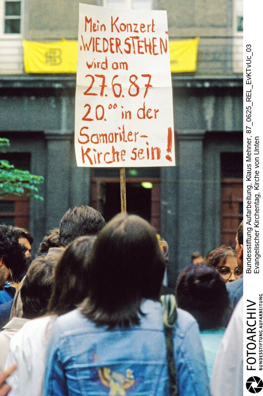 Opposition setzt Amtskirche unter Druck. Berlin (Bezirk Berlin) DDR, 25. 06. 1987. Foto: Mit Auftritts-Verbot belegter Liedermacher wirbt auf dem Gelände des Niederkirchner Gotteshauses für sein Konzert. Friedensgruppen und Mitglieder der Kirche von Unten halten der Amtskirche zu lasche Interventionen gegen Auflagen des Staatssekretariats für Kirchenfragen der DDR vor und organisieren ihren eigenen Kirchentag.<BR>Material/Technik: Foto<BR>Bezirk Berlin<BR>Signatur: 87_0625_REL_EvKTvUc_03