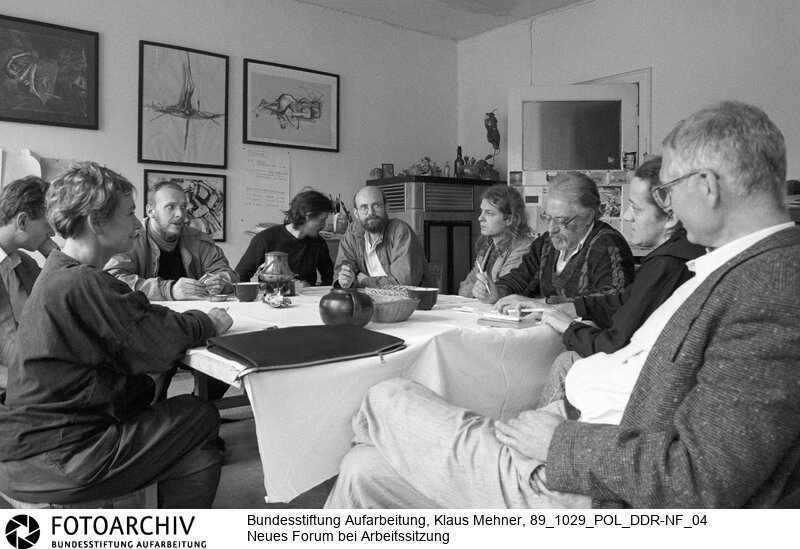 Foto (v.l.): Bärbel Bohley, Reinhard Schult, Michael Kukutz, Eberhard Seidel, Andreas Schönfelder, (nicht identifiziert), Hans-Joachim Tschiche, Jutta Seidel, Prof. Jens Reich bei Diskussion. Opposition und Regimekritiker organisieren sich. Berlin (Bezirk Berlin) DDR, 29. 10. 1989. Gründer und Mitglieder der regimekritischen Gründung Neues Forum trafen sich in der Wohnung einer Malerin zur Arbeitssitzung.<BR>Material/Technik: Foto<BR>Bezirk Berlin<BR>Signatur: 89_1029_POL_DDR-NF_04