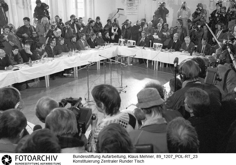 Konstituierung Zentraler Runder Tisch. Berlin (Bezirk Berlin) DDR, 07.12. 1989. Foto: Zentraler Runder Tisch bei konstituierender Sitzung. Einheitssozialisten und Opposition suchen den Dialog. Unter Supervision der Kirchen nehmen die etablierten Parteien und die Opposition im Bonhoeffer-Haus ihre Gespräche auf. Der Runde Tisch soll zum Kontrollgremium der Regierung während der Übergangsphase werden.<BR>Material/Technik: Foto<BR>Bezirk Berlin<BR>Signatur: 89_1207_POL-RT_23