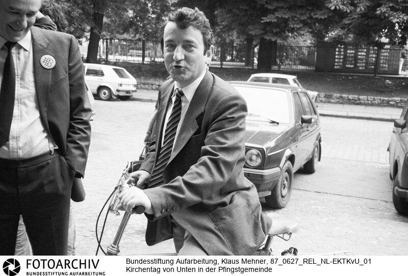 Foto: Kirchenanwalt Wolfgang Schnur (IM Thorsten, IM Dr. Schirmer) kam mit dem Radl. Berlin (Bezirk Berlin) DDR, 27. 06. 1987. Amtskirche toleriert Kirche von Unten. Aktivisten und Friedensgruppen hielten der Kirchenleitung zu lasche Interventionen gegen Auflagen des Staatssekretariats für Kirchenfragen vor und organisierten einen eigenen Kirchentag. Bild aus dem Bestand von Ralf Hirsch.<BR>Material/Technik: Foto<BR>Bezirk Berlin<BR>Signatur: 87_0627_REL_NL-EKTKvU_01