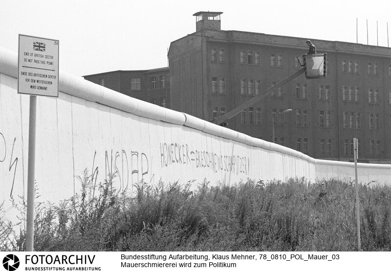 Berlin (Berlin West), 10. 08. 1978. Beschmierte Mauer wird zum Politikum. Die Deutsche Demokratische Republik (DDR) sorgt sich um das Aussehen des Antifaschistischen Schutzwalls. Da die Mauer durchgängig auf dem Territorium der DDR steht, protestiert Ostberlin bei dem Berliner Senat gegen Graffiti und politische Schmierereien an dem Bauwerk. Foto: Soldat der Grenztruppe bei Inspektion der Verschönerungen auf westlicher Seite.<BR>Material/Technik: Foto<BR>Berlin (West)<BR>Signatur: 78_0810_POL_Mauer_03
