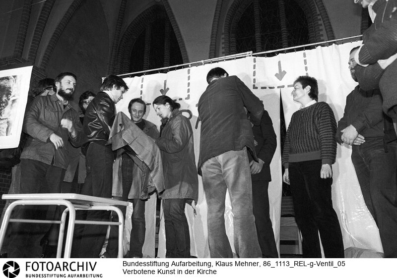 Berlin (Bezirk Berlin) DDR, 13-11-1986. Zum Auftakt der siebenten Friedensdekade verlieh der Pfarrer der evangelischen Samariter Gemeinde das Goldene Ventil an Aktivisten der Friedensbewegung. Anschließend boten im Beisein zahlreicher Mitarbeiter des Ministeriums für Staatssicherheit (MfS, Stasi) mit Auftrittsverbot belegte Künstler einen Farcenabend. Foto (v.l.n.r.): Verleihung des Goldenen Ventils an Wolfgang Templin, Rudi Pahnke (Brille, verdeckt), Ralf Hirsch, Rainer Dietrich (IM Cindy), Ulrike Poppe, Rainer Eppelmann (Rücken zur Kamera), Karin Bogan, Wolfgang Janisch in der Samariter Kirche. Copyright by: Klaus Mehner (Higher resolution available)<BR>Material/Technik: Foto<BR>Bezirk Berlin<BR>Signatur: 86_1113_REL-g-Ventil_05