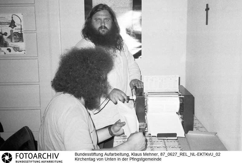 Foto: Manfred Rinke (HIM Raffelt) bei Produktion von Flugblättern. Berlin (Bezirk Berlin) DDR, 27. 06. 1987. Amtskirche toleriert Kirche von Unten. Aktivisten und Friedensgruppen hielten der Kirchenleitung zu lasche Interventionen gegen Auflagen des Staatssekretariats für Kirchenfragen vor und organisierten einen eigenen Kirchentag. Bild aus dem Bestand von Ralf Hirsch.<BR>Material/Technik: Foto<BR>Bezirk Berlin<BR>Signatur: 87_0627_REL_NL-EKTKvU_02