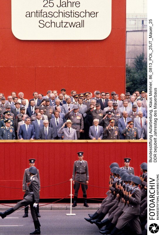 Foto: Nationale Volksarmee (NVA) bei Vorbeimarsch. Berlin (Bezirk Berlin) DDR, 13. 08. 1986. Jahrestag des Mauerbaus bejubelt. Mit einem Appell der Kampfgruppen (KG) beging die DDR den 25. Jahrestag des Mauerbaus. Der SED-Chef würdigte den antifaschistischen Schutzwall als Voraussetzung für die Friedens- und Entspannungspolitik. Partei- und Staatsführung nahmen den Vorbeimarsch von Nationaler Volksarmee und Betriebskampfgruppen ab.<BR>Material/Technik: Foto<BR>Bezirk Berlin<BR>Signatur: 86_0813_POL_25JT_Mauer_25